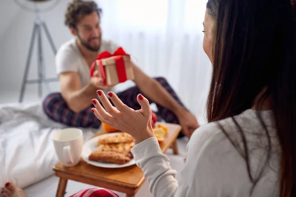 Jovem Dando Presente Natal Para Sua Namorada Animada Sentada Cama — Fotografia de Stock