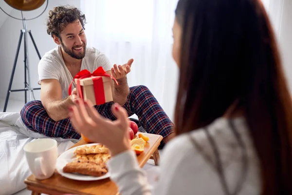 若い男は美しい休日の朝にベッドの中に存在するクリスマスによって彼のガールフレンドを驚かせた クリスマス 一緒に — ストック写真