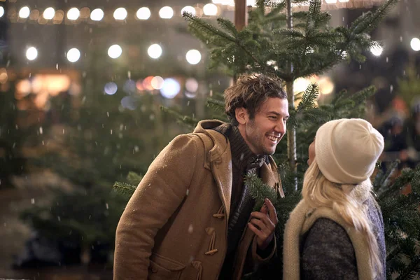 Genç, neşeli bir çift şehirde karlı bir havada büyülü bir gecede Noel ağacıyla eğleniyor. Noel ağacı, aşk, ilişki, Xmas, kar