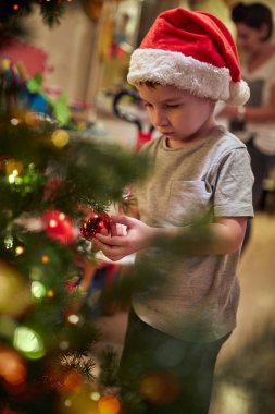 Tatil atmosferinde evde Noel ağacı süsleyen küçük bir çocuk. Birlikte, yeni yıl, aile, kutlama