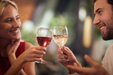 Güzel, genç, beyaz bir çift yemekte şarapla kadeh kaldırıyor, birbirlerine bakıp gülümsüyorlar.. 