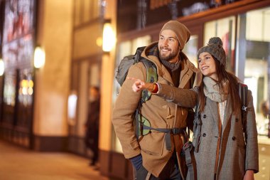 Genç bayan turist işaret parmağıyla başka bir yöne bakıyor, gülümsüyor. Yeni yıl tatilleri seyahat kavramı