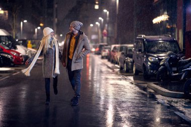 Genç bir çift boş bir yolun ortasında yürüyor, el ele tutuşuyor, birbirlerine bakıyor, gülümsüyor, gülüyor.