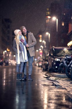 Kafkasyalı genç çift yukarı bakıyor, gülümsüyor, karın yağışını seyrediyor.