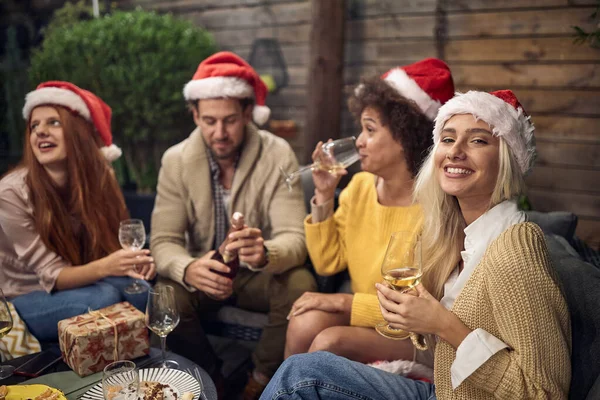 美しいブロンドはサンタの帽子をかぶっている友人とクリスマスを祝うカメラを見て白ワインを飲んで — ストック写真