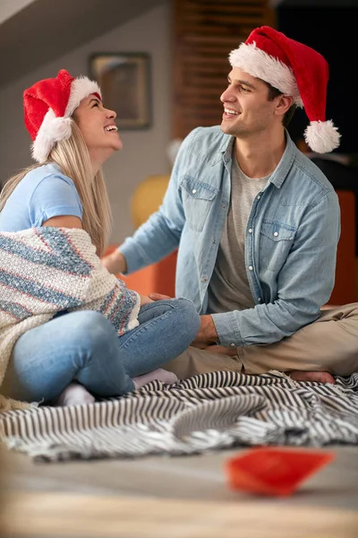 若い白人のカップルが家の床に座って笑ってサンタの帽子をかぶって — ストック写真