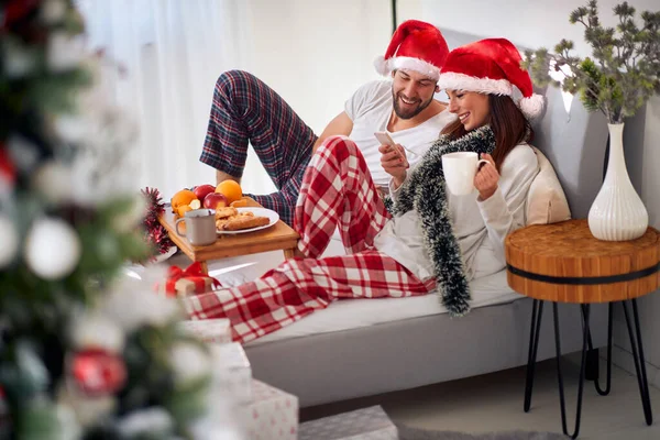 若い白人のカップルはクリスマスに悪い朝食を携帯電話を見て笑顔で — ストック写真