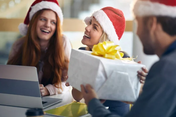 male colleague gives presents to female coworkers for christmas in the office