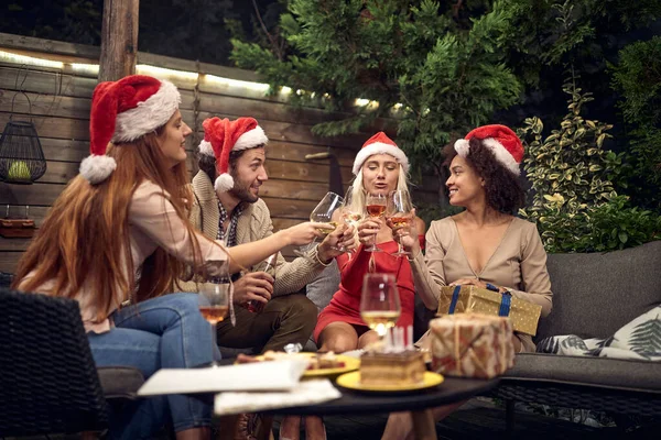 サンタの句の帽子でお祝い酒を飲む若い大人 — ストック写真