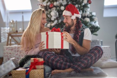 A young couple sitting at home excited about Xmas presents on a beautiful holiday morning. Christmas, relationship, love, together clipart