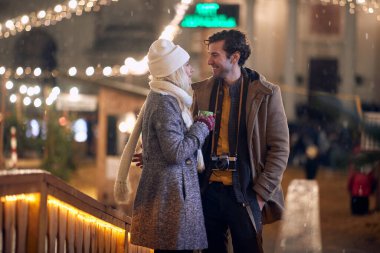 Noel zamanı genç beyaz bir çiftin romantik görüntüsü. Açık havada konuşuyorlar, birbirlerine yakın duruyorlar.