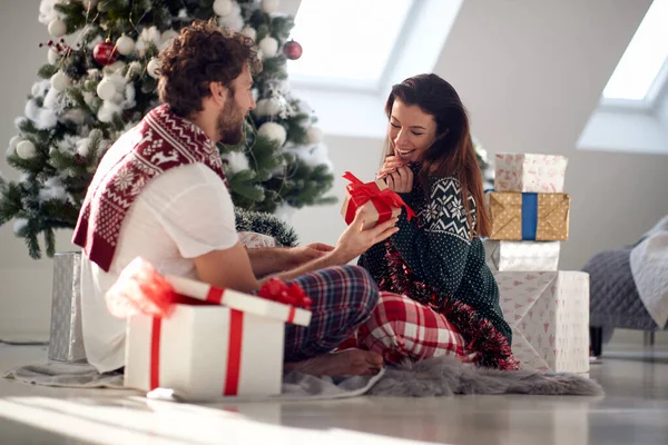 A boyfriend has a Xmas present for his girlfriend while together sitting on the floor on a beautiful holiday morning. Christmas, relationship, love, together