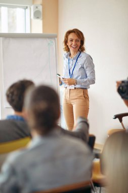 İş seminerinde başarı için Beyaz Kurul önünde gülümseyen beyaz kadın öğretim görevlisi.