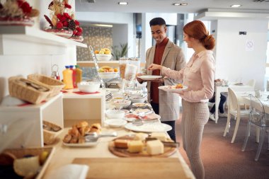 Genç beyaz kadın Afro-Amerikalı bir erkekle konuşuyor, tabağına yemek koyuyor, gülümsüyor, 