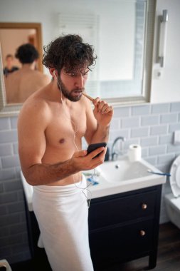 Genç yakışıklı bir adam, güzel bir banyoda dişlerini fırçalarken bir telefon alıyor. Hijyen, banyo, sabah