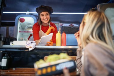 Fast food servisi önünde sandviç yiyen bir müşterinin tavsiyelerini dinleyen genç bir bayan.