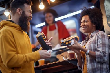 Arkadaşlar fast food servisi önünde sandviç yerken iyi vakit geçiriyorlar. Açık hava