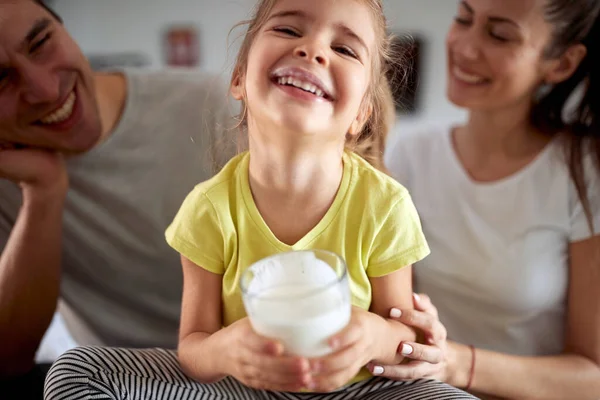 一个小女孩和她的父母在家里的家庭气氛中摆出一副带着一杯酸奶拍照的样子 一家人 一起吃早餐 一起回家 — 图库照片