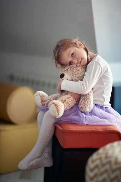 小さな女の子がベッドの上に抱っこしていると テディベアが家の気楽な雰囲気の中で写真のポーズをとっています — ストック写真