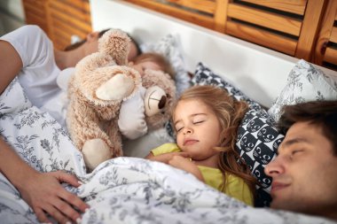 Mutlu ebeveynler yatakta çocuklarla birlikte uyuyorlar.