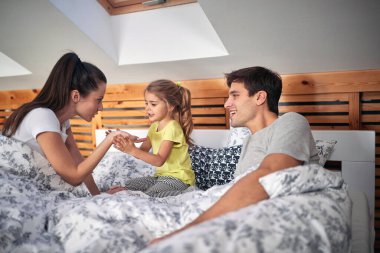 Mutlu ebeveynler yatakta kızlarıyla kucaklaşıyorlar.