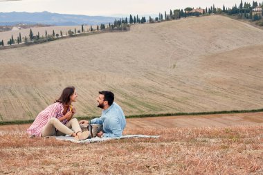 Genç bir çift geniş bir çayırda rahat bir atmosferde pikniğin tadını çıkarıyor. Aşk, ilişki, piknik, birlikte