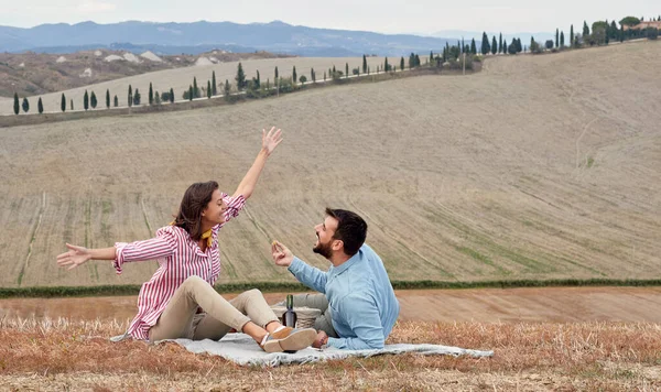 A young cheerful couple enjoying a talk while they have a picnic on a large meadow on a beautiful day. Love, relationship, picnic, together