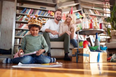 Evlat edinilmiş küçük çocuk yerde oturuyor ve neşeli bir atmosferde çocukların doğum günü partisinde oynuyor. Aile, kutlama, birlikte