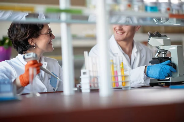 Young chemistry students are chatting while pipetting and microscoping in a laboratory in a relaxed atmosphere. Science, chemistry, lab, people