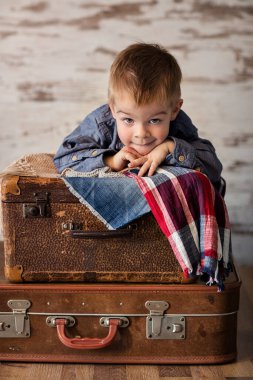 Kahverengi kırsal bavullara yaslanan küçük şirin çocuk.