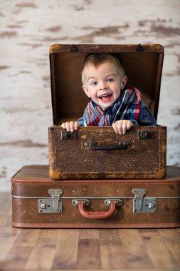 Komik küçük çocuk kırsal bir bavulda oturuyor.