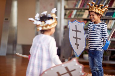 Küçük bir erkek ve kız kardeş şövalye gibi giyinmiş evde neşeli bir atmosferde oynarken kılıç savaşı yapıyorlar. Aile, ev, oyun zamanı
