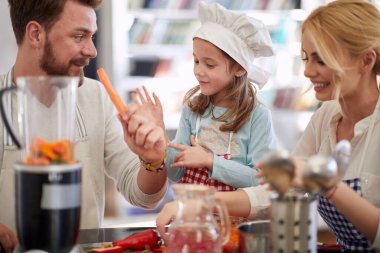 Genç bir aile, evde neşeli bir atmosferde birlikte hazırladıkları bir yemek için sebzeleri hazırlıyor. Aile, ev, mutfak.