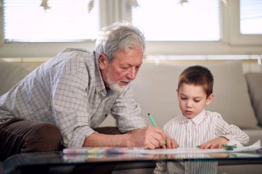 Bir dede, torununa evde rahat bir atmosferde nasıl resim çizileceğini gösteriyor. Aile, ev, oyun zamanı