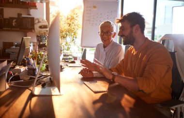 Genç bir iş adamı, iş yerindeki hoş bir ortamda yaşlı bir meslektaşına bilgisayar ekranı içeriğini gösteriyor. İş, ofis, iş