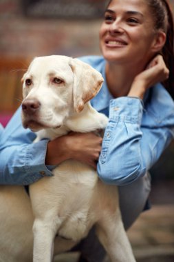Genç ve güzel bir kız, güzel bir günde köpeğiyle kucaklaşıp poz veriyor. Boş zaman, bar, arkadaşlık, açık hava.