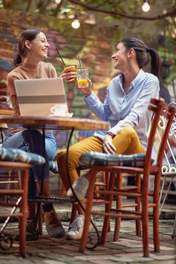 Two female friends toasting while having a drink in a cheerful atmosphere at the bar. Leisure, bar, friendship, outdoor