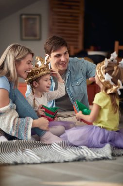 Genç ve mutlu bir aile yerde oturuyor ve evde rahat bir atmosferde birlikte oynuyorlar. Aile, oyun, ev, birliktelik.
