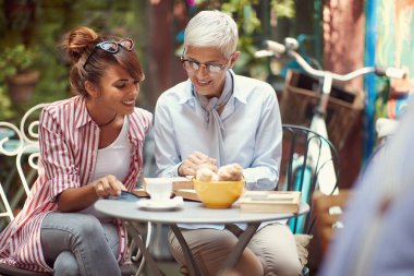 Genç bayan arkadaşıyla birlikte kitap okuyan yaşlı bir kadın barda rahat bir atmosferde kahve içerken. Boş zaman, bar, arkadaşlık, açık hava.