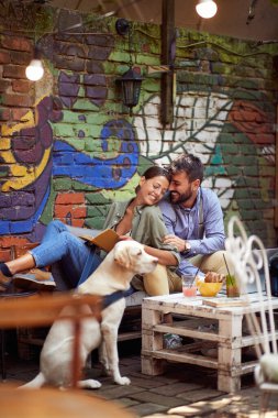 A young couple in love spending a wonderful time in a relaxed atmosphere at a bar together with their dog. Leisure, bar, friendship, outdoor