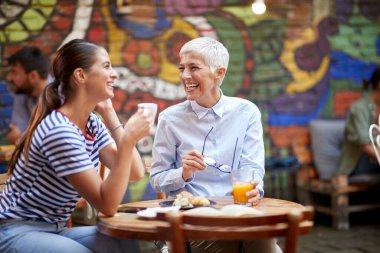 Two happy female friends of different generations having a good time while they have a drink in a cheerful atmosphere in the bar. Leisure, bar, friendship, outdoor