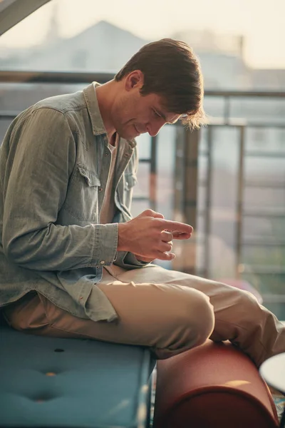 一个年轻人一边用他的智能手机一边在舒适的家庭氛围中放松 — 图库照片