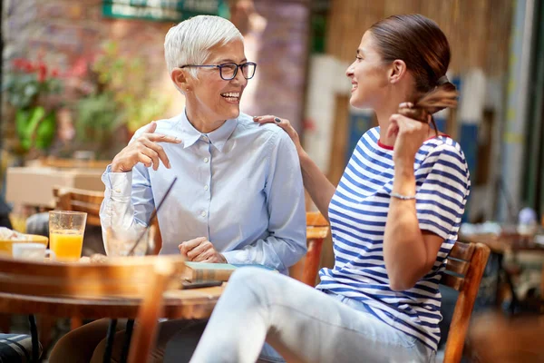 Two female friends of different generations have a friendly talk while they have a drink in a pleasant atmosphere in the bar. Leisure, bar, friendship, outdoor