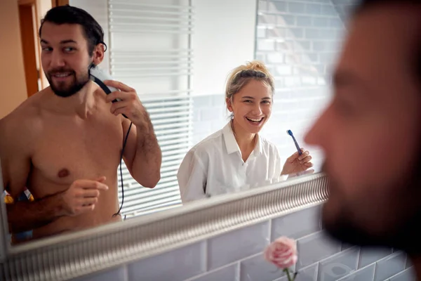 若い男が髭を剃り女に歯を洗っていた 笑顔鏡を見て — ストック写真