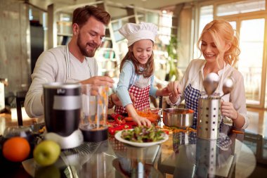 A little daughter helping her parents in meal preparation in a cheerful atmosphere at home. Family, together, home