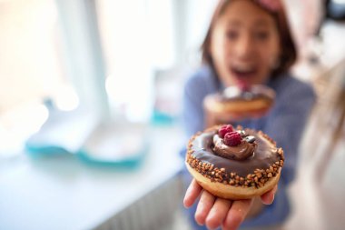Elinde karşı konulmaz çikolatalı bir çörek tutan ve bir pastanede hoş bir atmosferde poz veren bir kızın yakın çekimi. Pastane, tatlı, tatlı