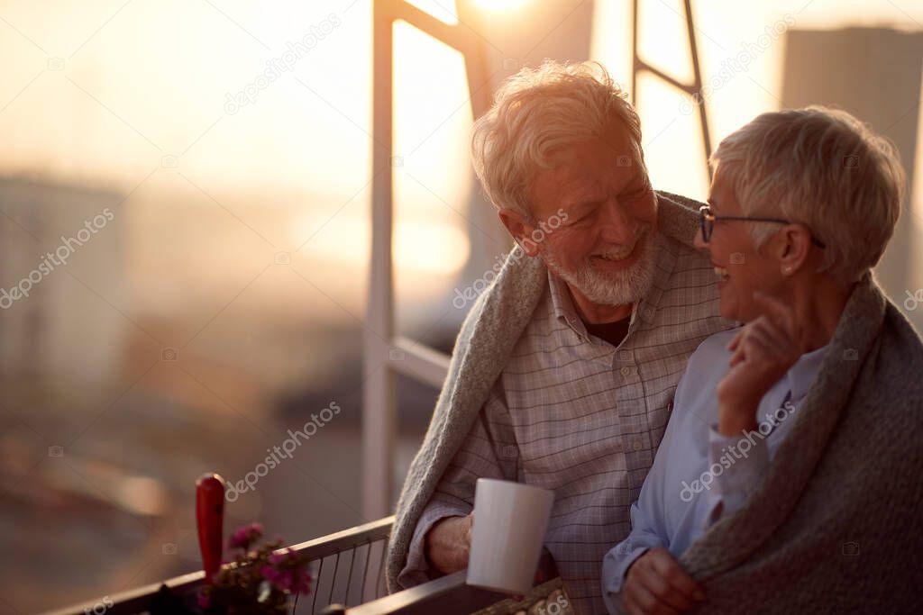 An elderly couple having a good time together on the terrace of their apartment at a beautiful sunset. Spouses, pensioners, together, home