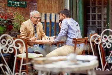 Yaşlı bir adam ve genç arkadaşı barda neşeli bir atmosferde satranç oynarken iyi vakit geçiriyorlar. Boş zaman, bar, arkadaşlık, açık hava.