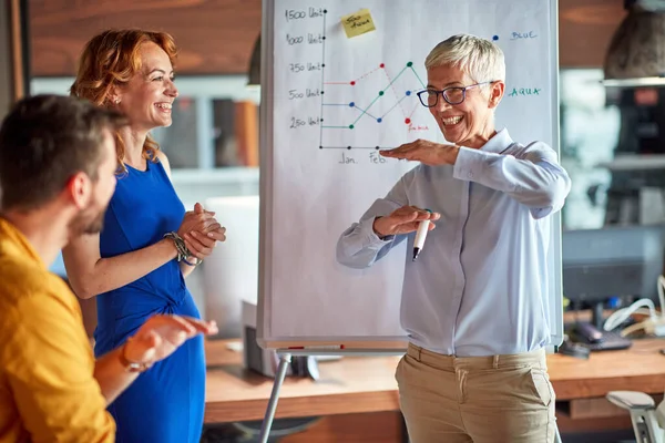 An older business woman giving an explanation to her colleagues during a presentation in a pleasant atmosphere at workplace. Business, office, job