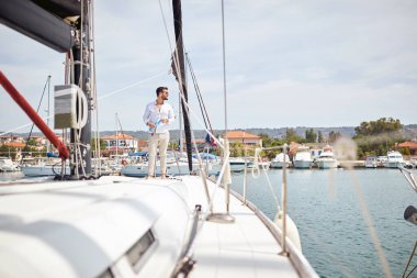 Genç yakışıklı bir adam yatta duruyor ve güzel güneşli bir günde deniz kenarında gezintiden zevk alıyor. Yaz, deniz, tatil